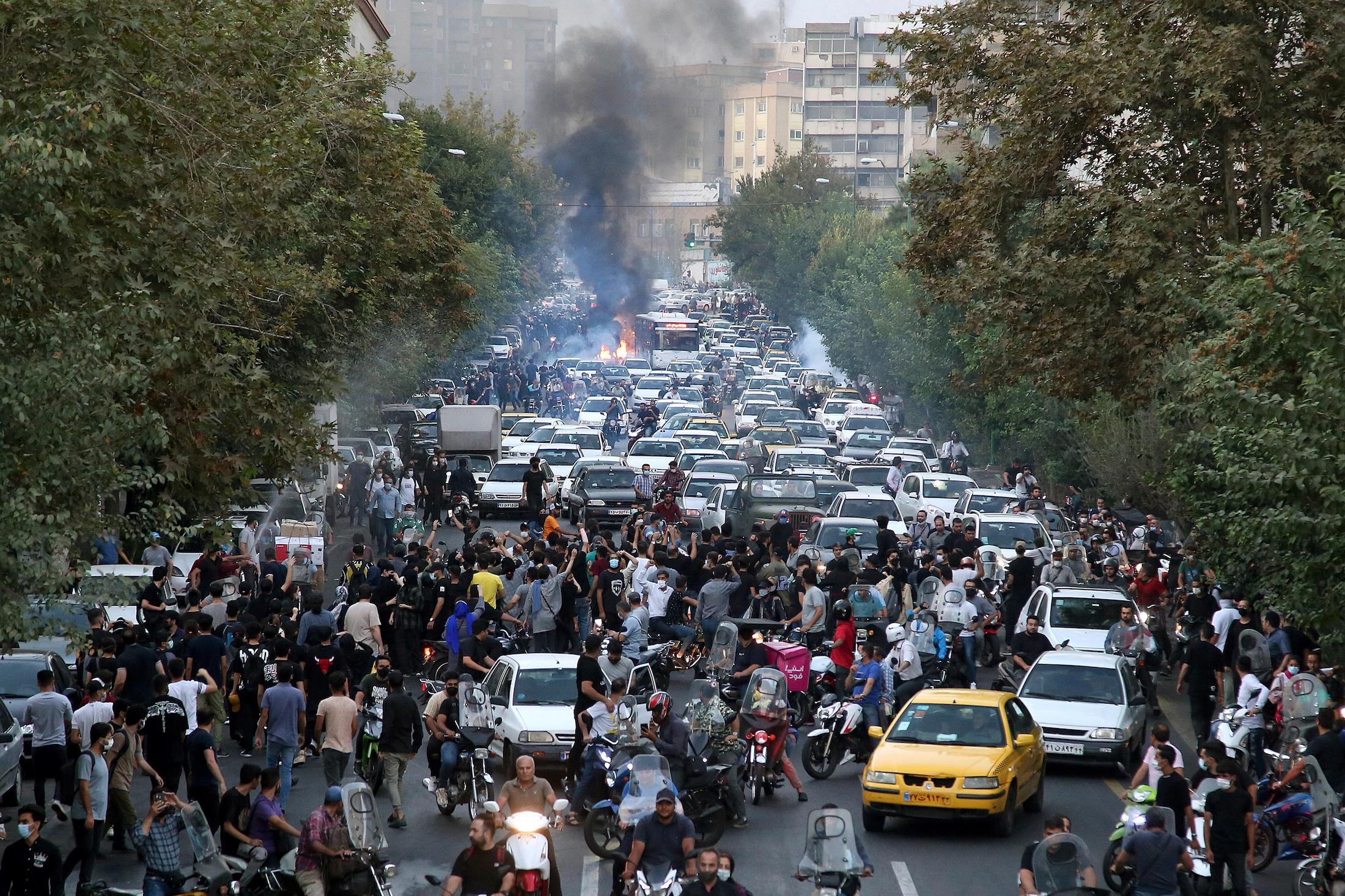 Mass protests erupt on the streets of Iran with smoke rising and crowds filling the road amid escalating tensions